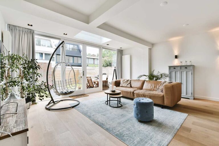 A person cleaning a bright, well-lit living room with minimal furniture and tidy decor.
